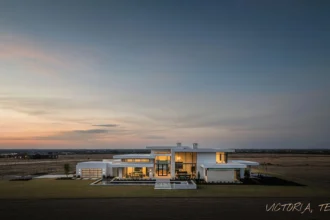 Modern luxury home in Victoria, Texas at sunset with glowing interior lights and open prairie backdrop