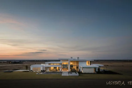Modern luxury home in Victoria, Texas at sunset with glowing interior lights and open prairie backdrop