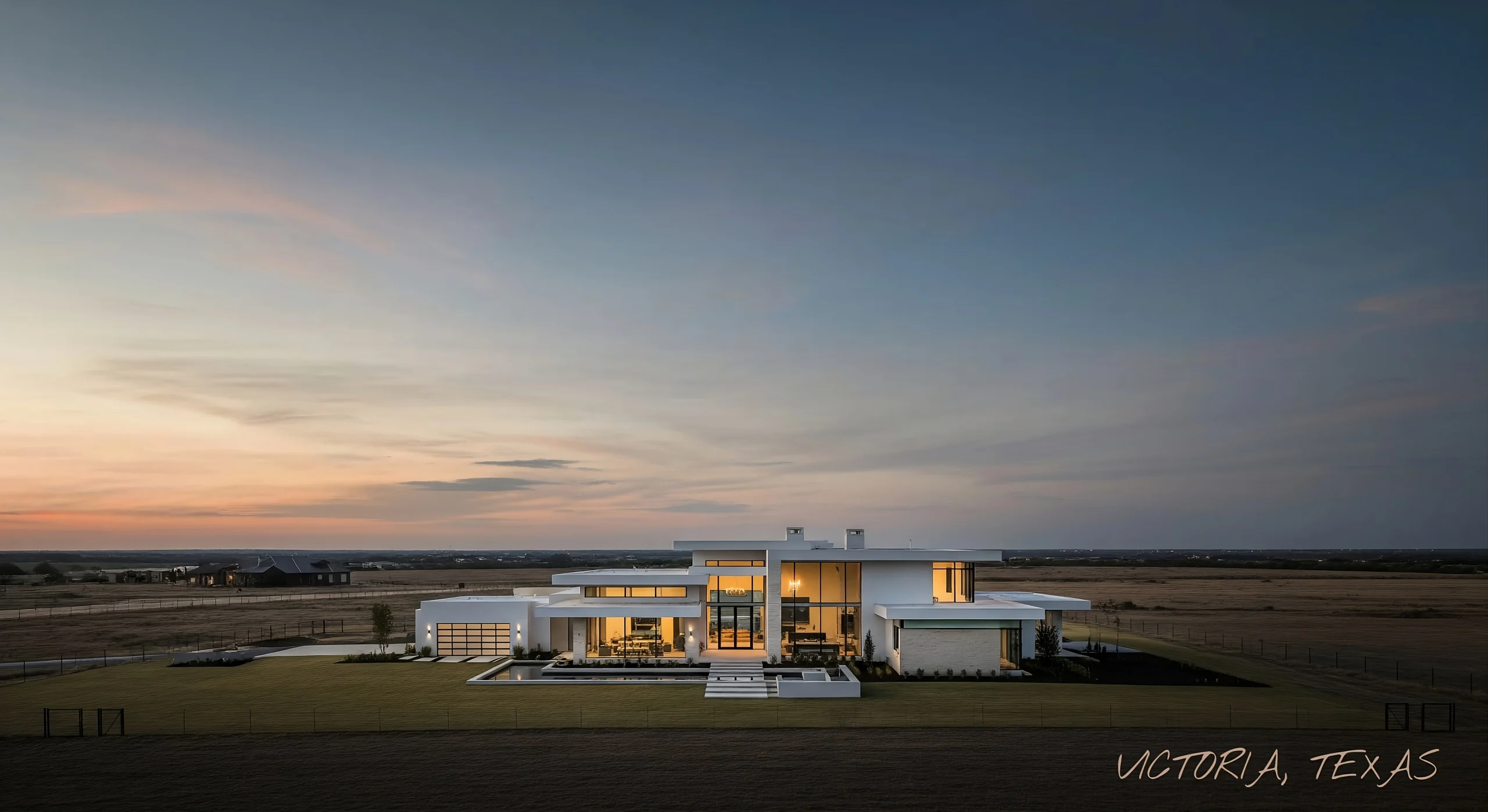 Modern luxury home in Victoria, Texas at sunset with glowing interior lights and open prairie backdrop