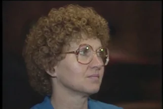 A close-up, slightly grainy photo of Candy Montgomery with tight, light brown curly hair and large, light-rimmed glasses, looking off to the side.